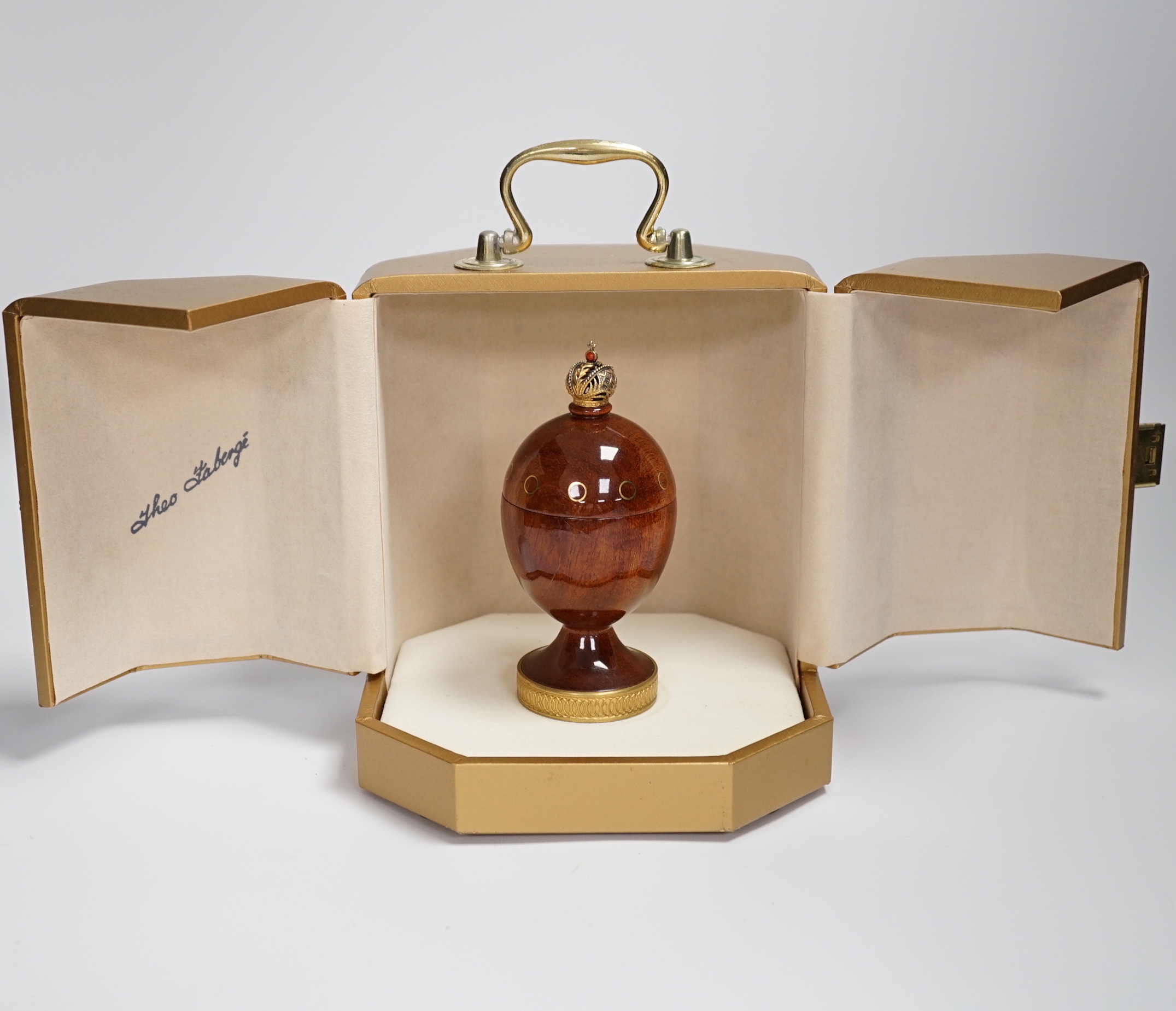 A cased Theo Faberge, (1922-2007) turned bubinga wood Eternity Egg, with Imperial Crown finial, gilt ring decoration and interior blackwood ring tray, with box and paperwork, 13.1cm